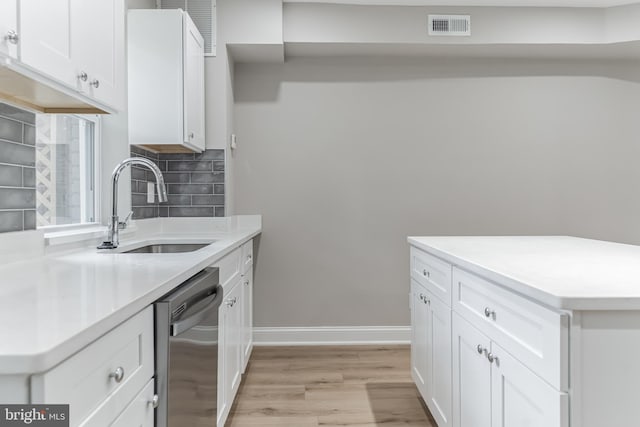 kitchen featuring light hardwood / wood-style flooring, backsplash, white cabinetry, stainless steel dishwasher, and sink