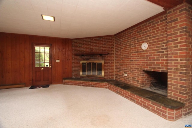 unfurnished living room featuring brick wall, wooden walls, carpet floors, and a brick fireplace