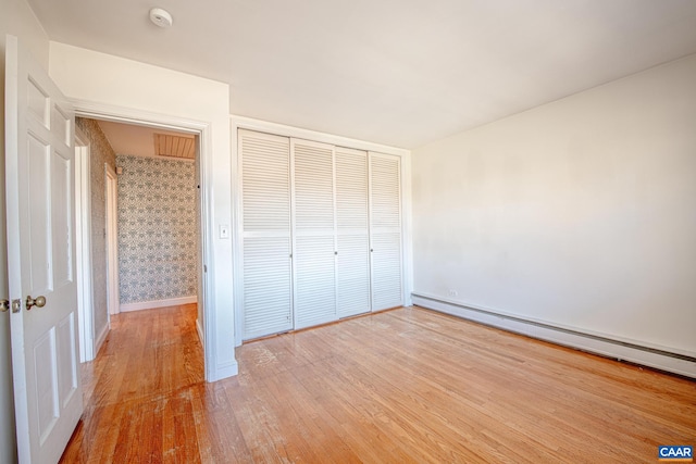 unfurnished bedroom featuring hardwood / wood-style flooring, a closet, and baseboard heating