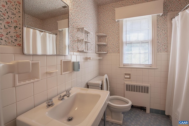 bathroom featuring radiator, tile walls, walk in shower, sink, and toilet