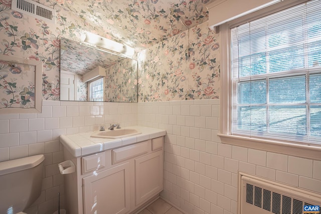 bathroom featuring a wealth of natural light, vanity, radiator heating unit, and tile walls