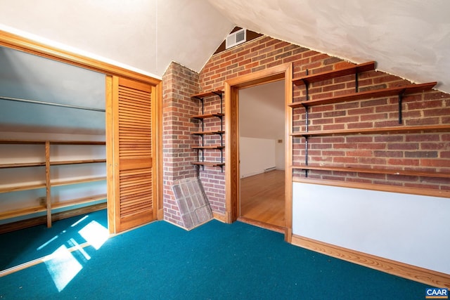 unfurnished bedroom featuring carpet flooring, brick wall, and vaulted ceiling