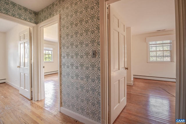 hallway featuring light wood-type flooring, a healthy amount of sunlight, and a baseboard radiator