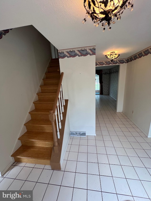 staircase featuring a notable chandelier, a textured ceiling, and light tile floors