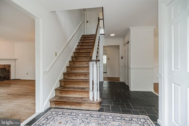 stairs with dark wood-type flooring, a fireplace, and ornamental molding