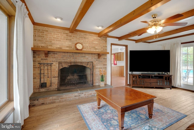 living room featuring ceiling fan, beamed ceiling, a brick fireplace, and light hardwood / wood-style floors