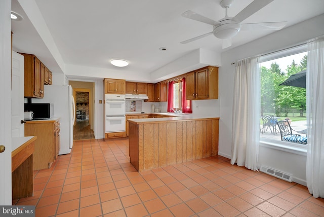 kitchen with kitchen peninsula, ceiling fan, white appliances, and light tile patterned floors