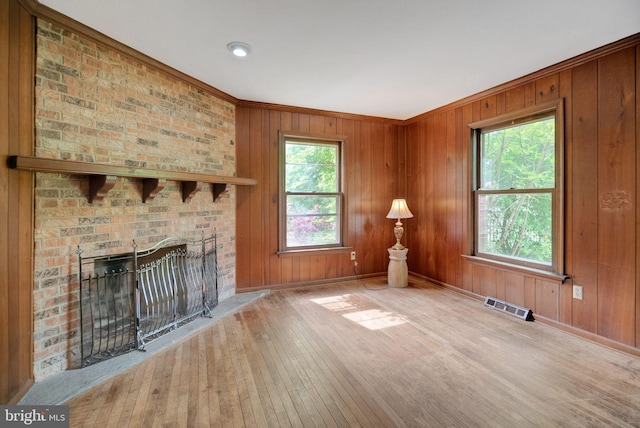 unfurnished living room featuring crown molding, wooden walls, a brick fireplace, brick wall, and hardwood / wood-style floors