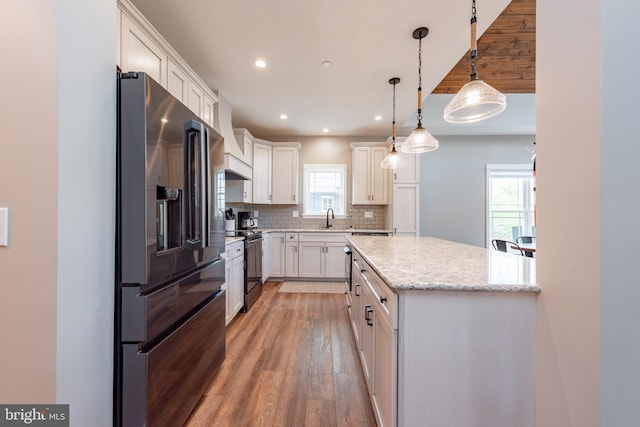 kitchen with high end refrigerator, hanging light fixtures, light hardwood / wood-style floors, tasteful backsplash, and white cabinets