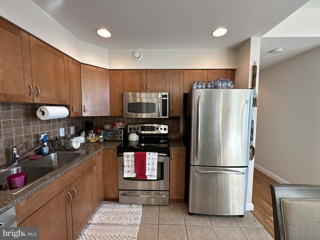 kitchen with light hardwood / wood-style flooring, backsplash, dark stone countertops, appliances with stainless steel finishes, and sink