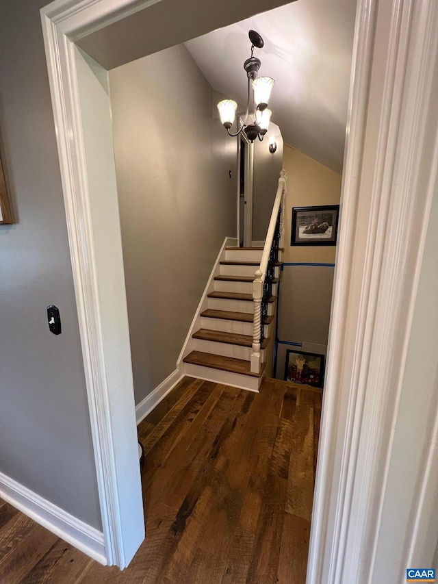 stairway with a chandelier, wood-type flooring, and lofted ceiling