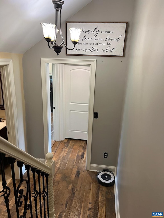 hall with lofted ceiling, dark wood-type flooring, and an inviting chandelier