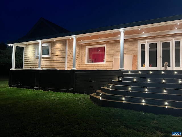 property exterior at night featuring a yard and french doors