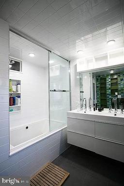 bathroom featuring combined bath / shower with glass door, oversized vanity, tile walls, and dual sinks