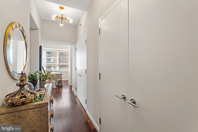 corridor with a notable chandelier, vaulted ceiling, and dark wood-type flooring