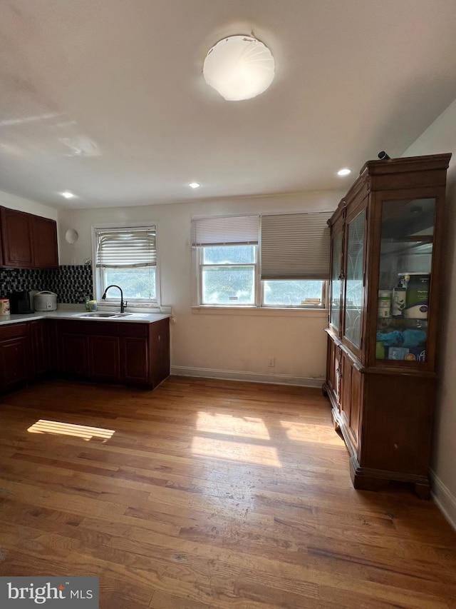 kitchen with dark brown cabinets, sink, light hardwood / wood-style flooring, and backsplash