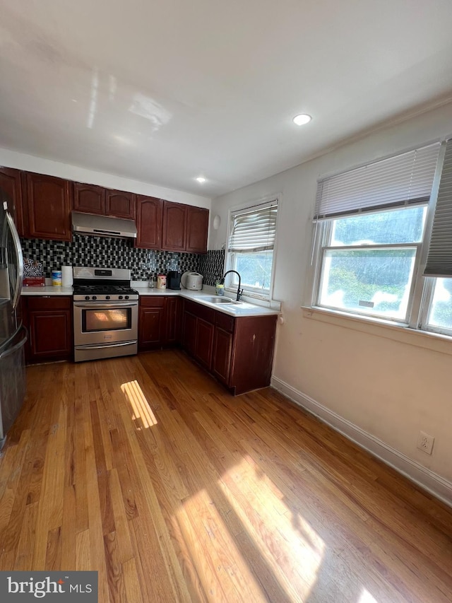 kitchen with appliances with stainless steel finishes, backsplash, hardwood / wood-style flooring, and a healthy amount of sunlight