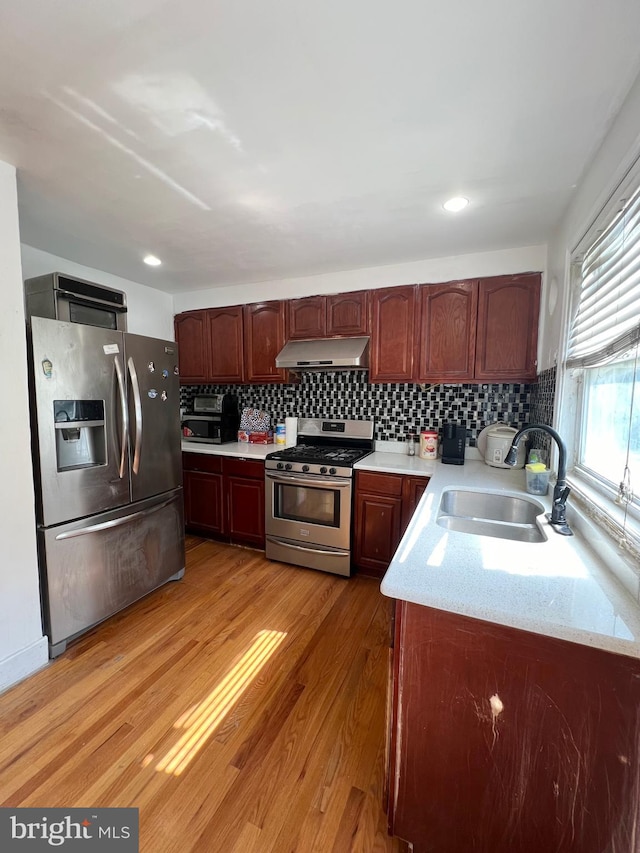 kitchen with light stone countertops, backsplash, light hardwood / wood-style flooring, stainless steel appliances, and sink