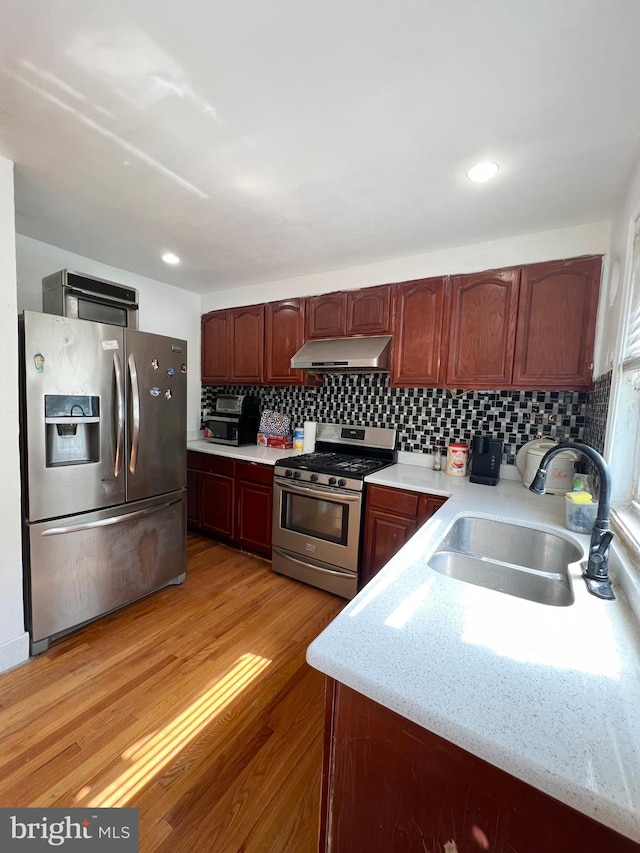 kitchen featuring light stone countertops, light wood-type flooring, backsplash, appliances with stainless steel finishes, and sink