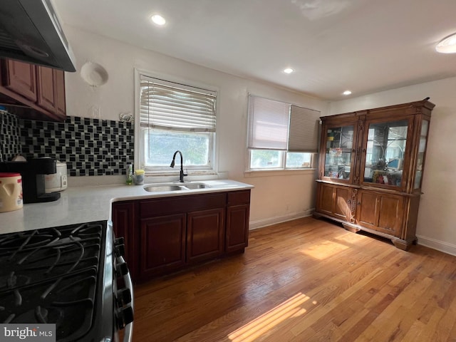 kitchen featuring wall chimney exhaust hood, sink, backsplash, stove, and light hardwood / wood-style flooring