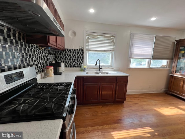 kitchen featuring stainless steel range with gas stovetop, wall chimney exhaust hood, sink, backsplash, and light wood-type flooring