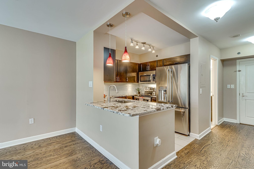 kitchen featuring light stone countertops, appliances with stainless steel finishes, decorative light fixtures, sink, and kitchen peninsula