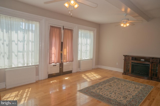 unfurnished living room featuring radiator heating unit, light wood-type flooring, ceiling fan, and beam ceiling