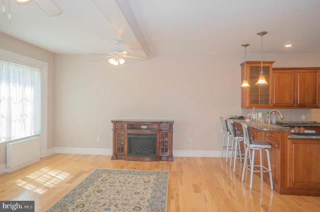 kitchen with tasteful backsplash, decorative light fixtures, light hardwood / wood-style floors, a kitchen bar, and radiator heating unit