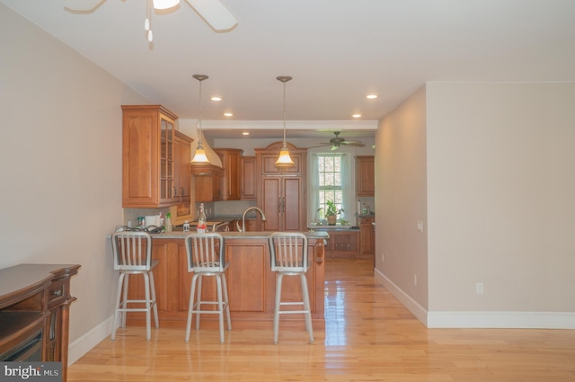 kitchen with sink, hanging light fixtures, light hardwood / wood-style floors, kitchen peninsula, and a breakfast bar area