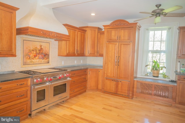 kitchen with light wood-type flooring, custom range hood, ceiling fan, double oven range, and beamed ceiling