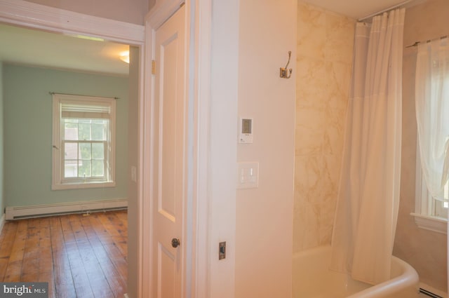 interior space with hardwood / wood-style floors, a baseboard radiator, and shower / tub combo