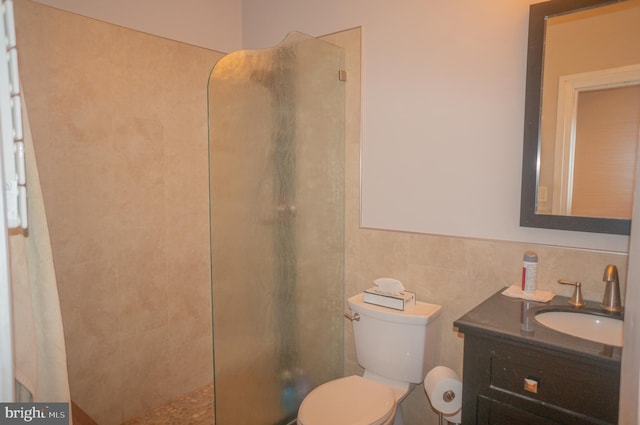 bathroom with vanity, toilet, a tile shower, and tile walls