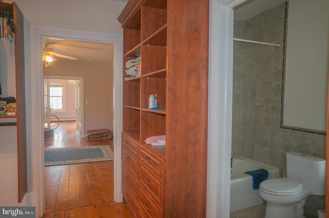 interior space with ceiling fan, tiled shower / bath combo, wood-type flooring, toilet, and tile walls