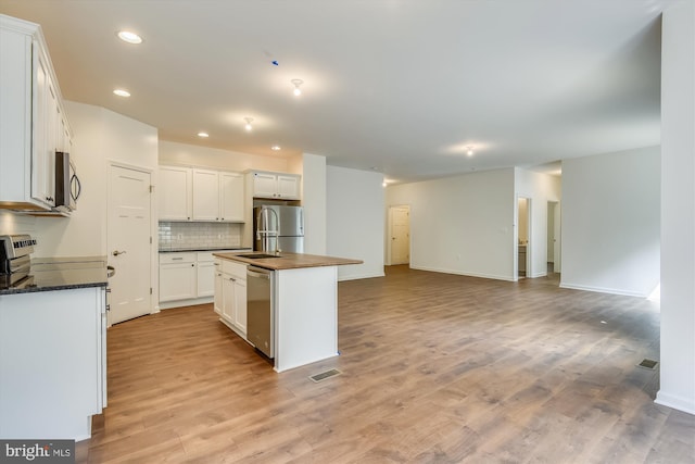 kitchen featuring backsplash, stainless steel appliances, a center island with sink, light hardwood / wood-style floors, and white cabinetry