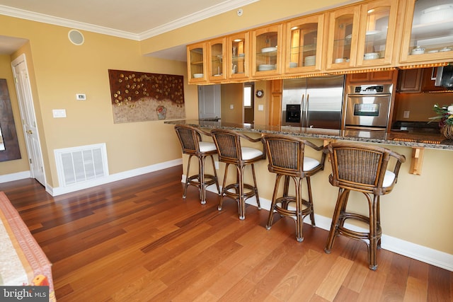 kitchen with crown molding, hardwood / wood-style floors, stainless steel appliances, a kitchen bar, and dark stone countertops