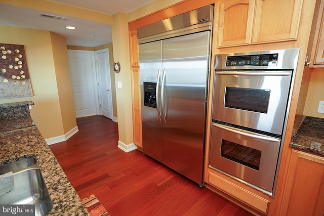 kitchen featuring appliances with stainless steel finishes, dark hardwood / wood-style floors, sink, and dark stone countertops