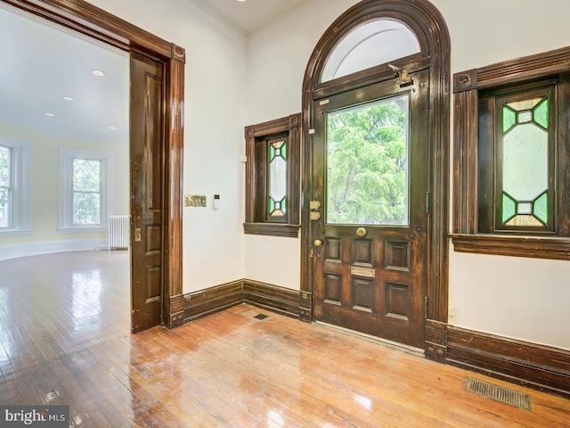 entryway with wood-type flooring, crown molding, and radiator