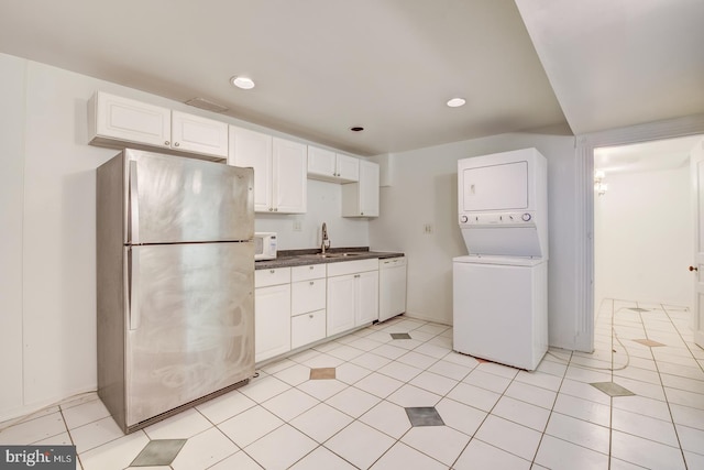 kitchen featuring light tile patterned floors, white appliances, stacked washing maching and dryer, and white cabinetry