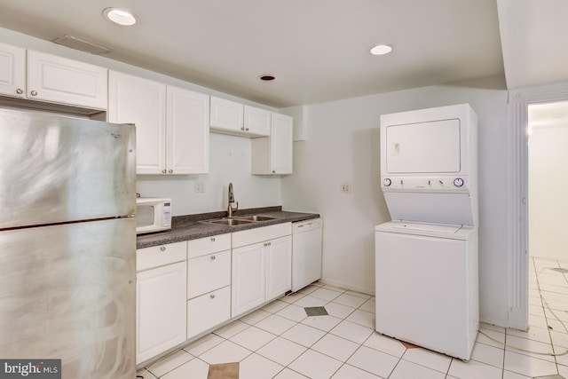 kitchen featuring white appliances, stacked washer and clothes dryer, white cabinets, sink, and light tile patterned floors