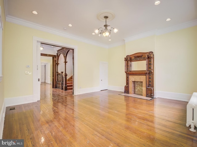 unfurnished living room featuring crown molding, a fireplace, hardwood / wood-style floors, and an inviting chandelier