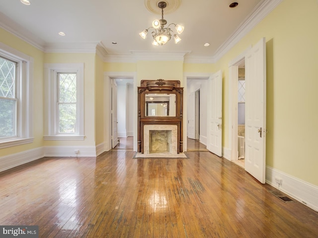 unfurnished living room with hardwood / wood-style floors, a premium fireplace, crown molding, and an inviting chandelier