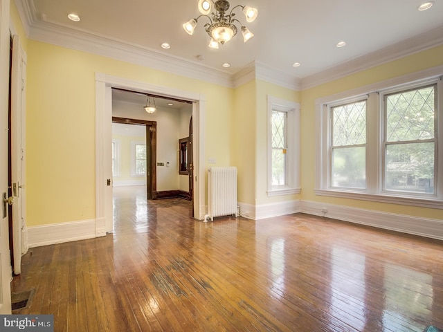 unfurnished room with hardwood / wood-style floors, radiator heating unit, ornamental molding, and an inviting chandelier