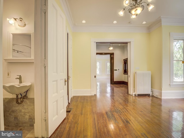 corridor with radiator heating unit, sink, dark wood-type flooring, an inviting chandelier, and ornamental molding