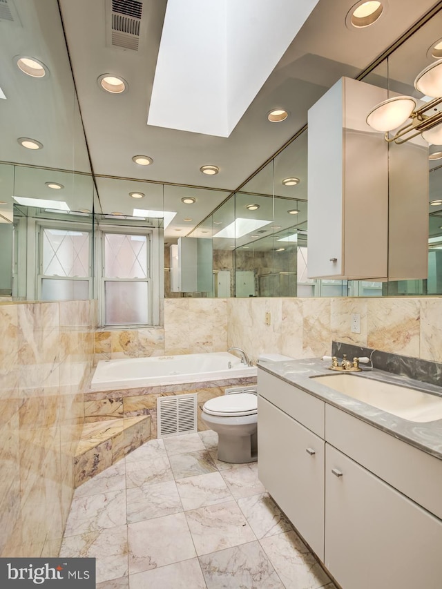 bathroom with a relaxing tiled tub, toilet, vanity, and a skylight