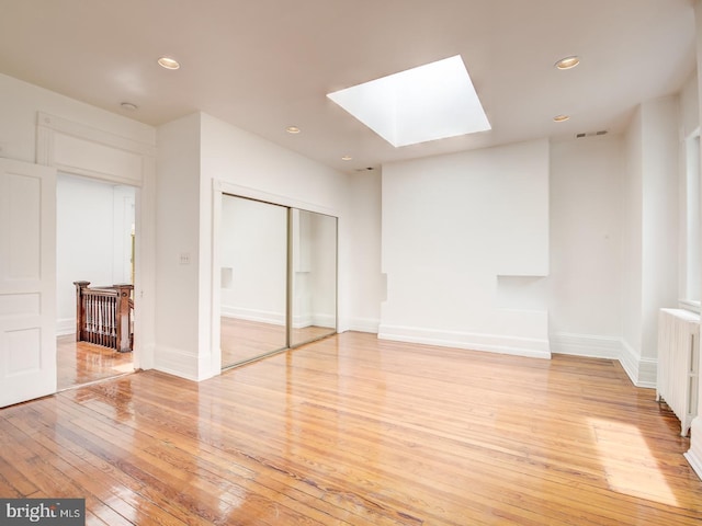 interior space featuring a skylight, a closet, radiator heating unit, and light wood-type flooring