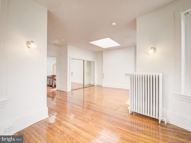 unfurnished room featuring radiator, a skylight, and light hardwood / wood-style floors