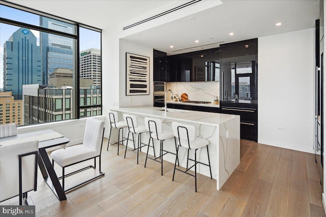 kitchen featuring light hardwood / wood-style flooring, a breakfast bar area, gas stovetop, tasteful backsplash, and sink