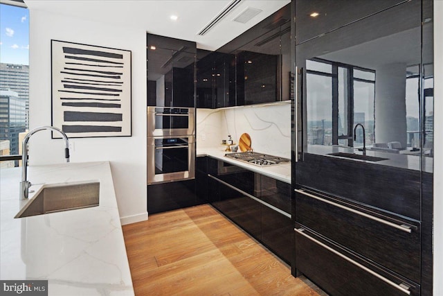 kitchen featuring sink, tasteful backsplash, light hardwood / wood-style flooring, and appliances with stainless steel finishes