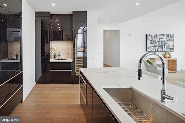 kitchen with dark brown cabinets, sink, light hardwood / wood-style floors, and light stone counters