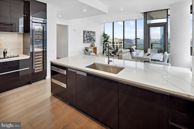 kitchen featuring light stone countertops, dishwashing machine, light hardwood / wood-style flooring, a wall of windows, and sink